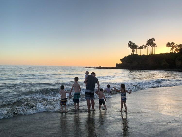 Joseph and the 5 children are seen from behind walking along the sea front with the sun setting in front of them