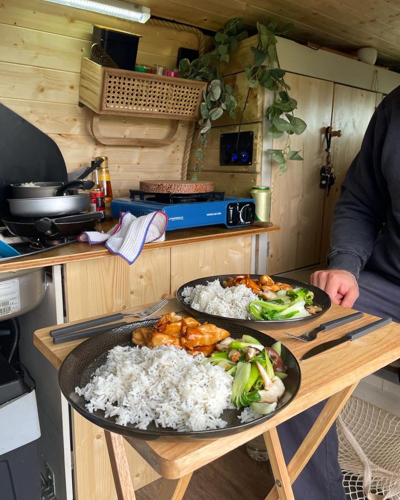 2 plates on a table inside the campervan. They have sticky chicken, rice and pak choy