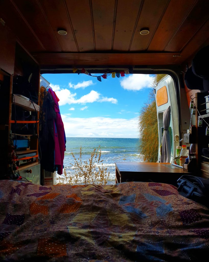 Looking out from the bed in the van, the back doors are open and the sea is in the background.