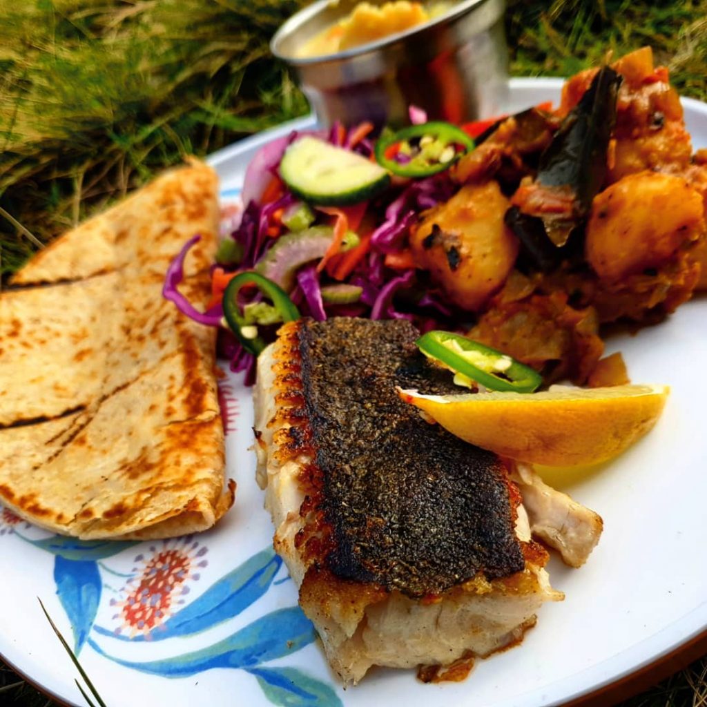 Plate of food in the sunshine. Charred fish, folded wrap and roasted vegetables.