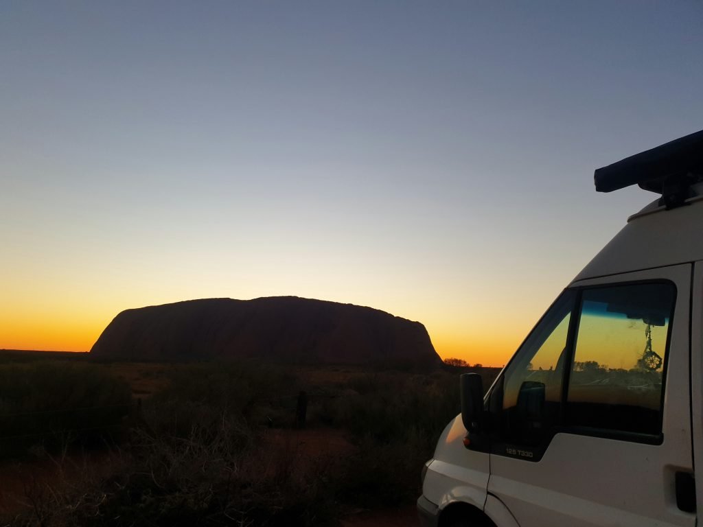 Vinny the van in the foreground of the photo with a sunset behind a large rock in the background.