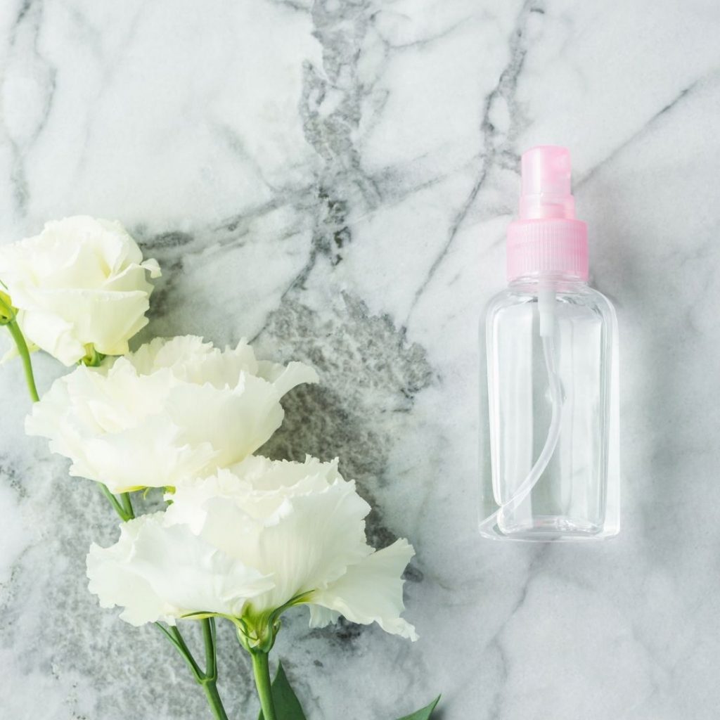 Re-useable plastic spray bottle with white flowers lying next to it