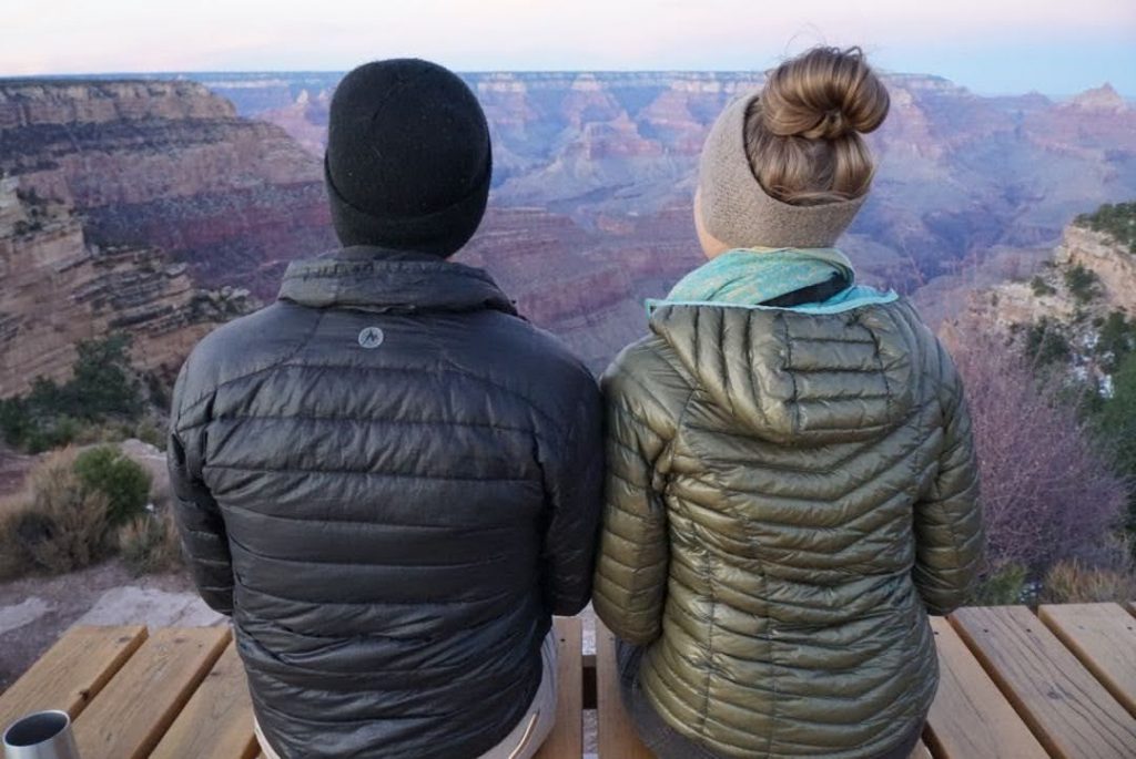 Andy & Ayana with their backs to the camera. Sat on the roofdeck of the van looking into a canyon.